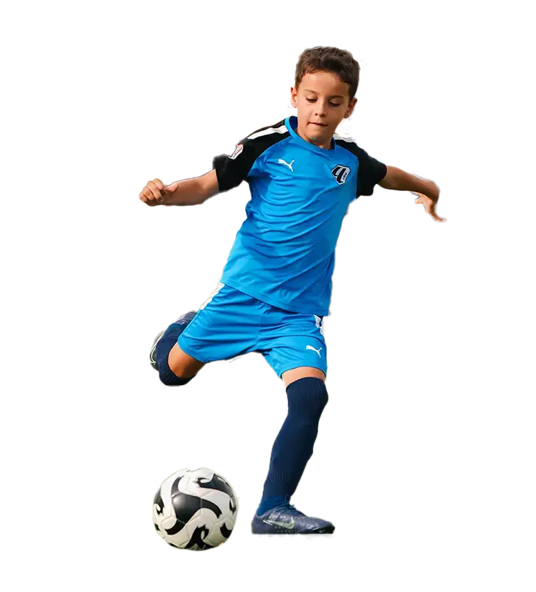 A young boy energetically kicks a soccer ball on a vibrant field, showcasing his skills during LaLiga Academy Dubai trials. Soccer Skills on Display | LaLiga Academy Dubai Open Trials
