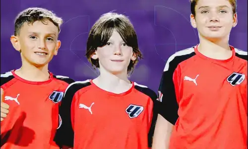 Three young boys in red and black soccer uniforms, representing football classes near me. Three Young Boys in Red and Black Soccer Uniforms | Football Classes Near Me
